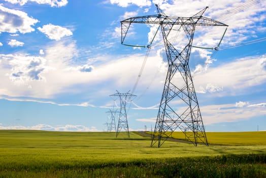 Power lines in a farm field on a sunny day with clouds