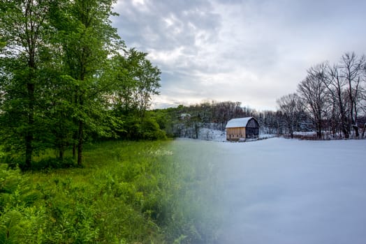 Transition photo from summer to winter of barn and trees in field