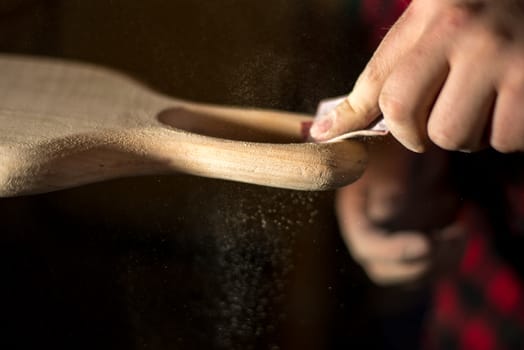 Hands manual sanding a wood cutting board handle