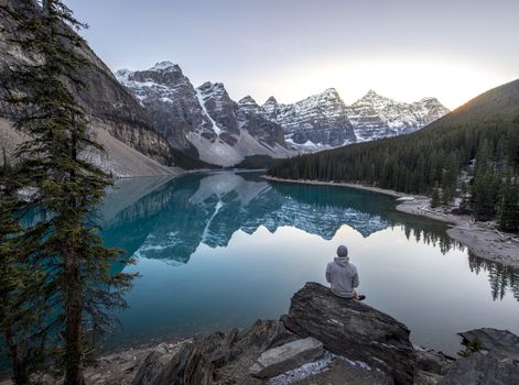 Young man sitting on a rock overlooking a beautful blue mountain lake