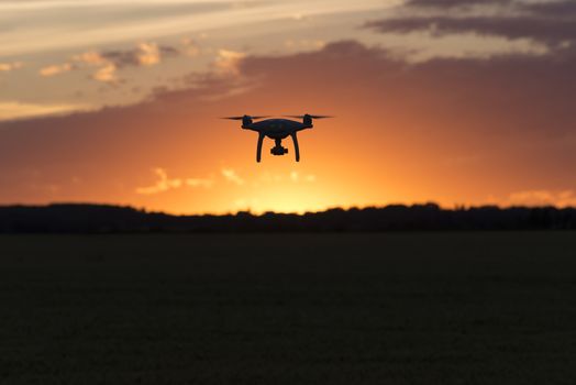 Drone silhouetted against orange sunset taking video