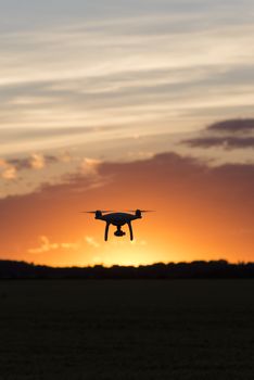 Drone silhouetted against orange sunset taking video