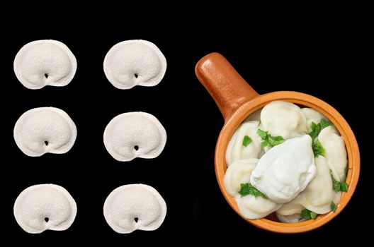 Boiled and some raw dumplings with greens and sour cream isolated on black background. The view from the top.