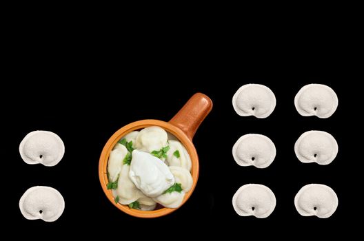Dumplings with greens and sour cream in a ceramic bowl isolated on black background. bit, top view.