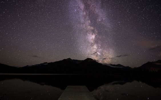 Milky way rising over a dock in water with mountains