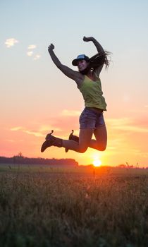 Cowgirl jumping for joy in a field at sunset
