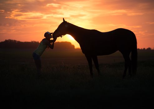Girl kissing her horse at sunset in a field
