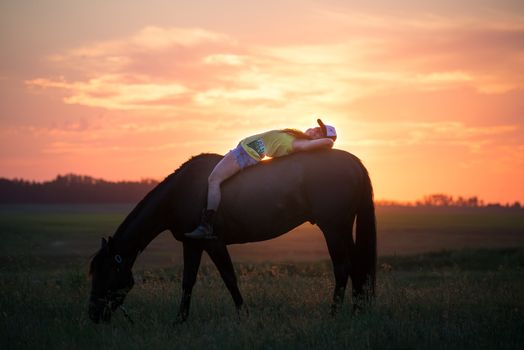 Girl lying on her horse without a sadle relaxing while it eats grass