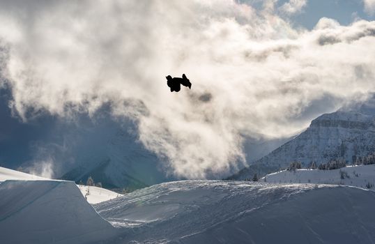 Snowboarder performing a flip off a large jump in the mountains