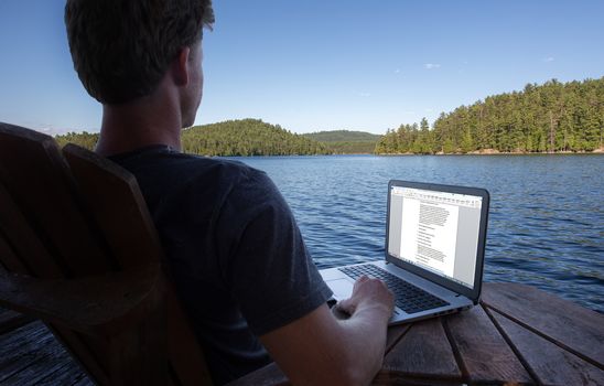 Young caucasian man working on laptop while on vacation to the lake
