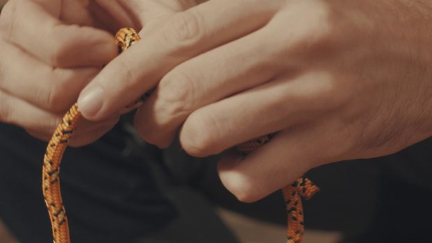 Man's hands tying a mountaineering knot on a rope. Close up.