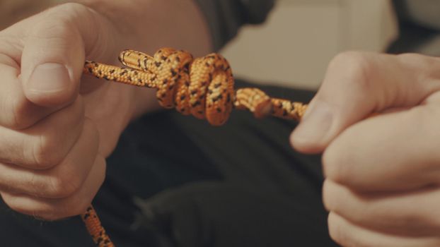 Man's hands tying a mountaineering knot on a rope. Close up.