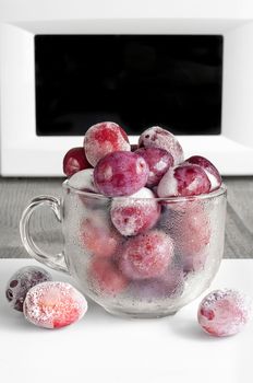 Frozen plums in a glass Cup on the background of the microwave.