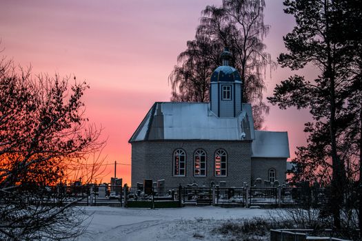 Small Christian church in the village at sunset. Winter times