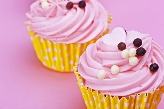 Two sweet cupcake with chocolate balls isolated on a pink background 