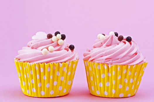 Two sweet cupcake with chocolate balls isolated on a pink background 