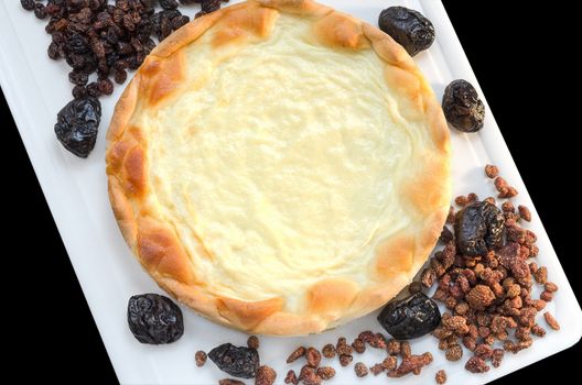 Cream pie and dried fruit on a white chopping Board, isolated black background.