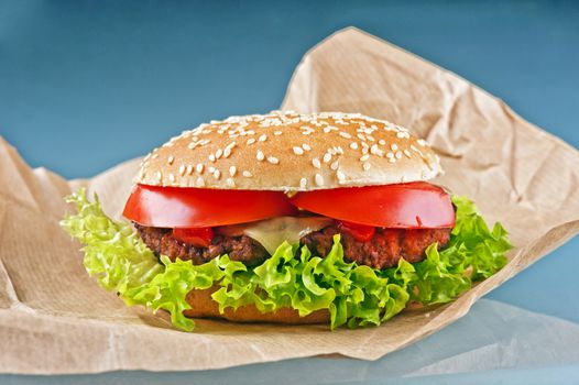 Tasty cheeseburger with tomatoes and fresh green lettuce on blue background