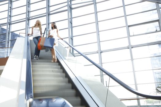 Young beautiful happy women on escalator of shopping mall