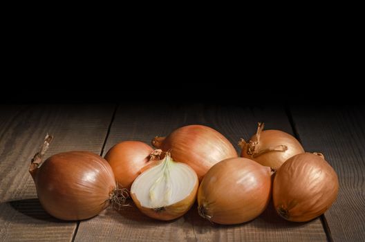 Raw onion is laying on an old wooden table and a black background. Plenty of space for text.