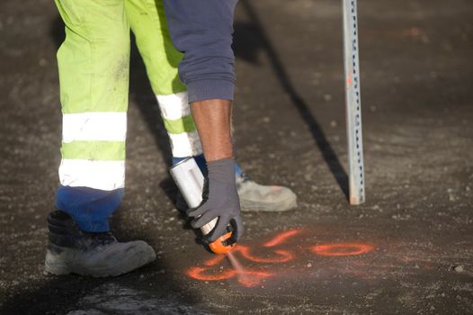 Worker marks a spot on asphalt with florescent spray paint in preparation for widening a road
