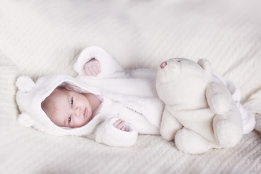 Beautiful sleepy newborn baby girl in white bear overalls on bed