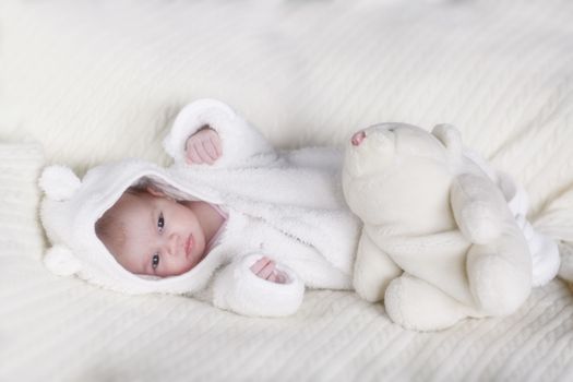 Beautiful sleepy newborn baby girl in white bear overalls on bed