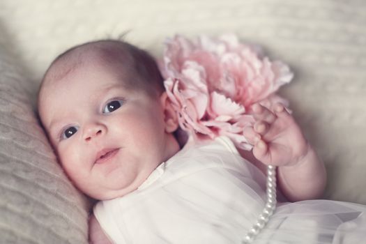 Newborn baby girl in fashionable dress with flower and pearl beads