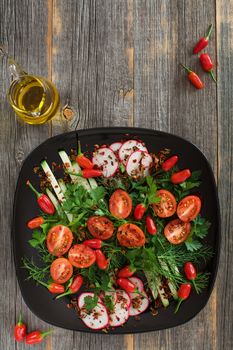 Greens and vegetables salad on a black ceramic plate and old wooden boards