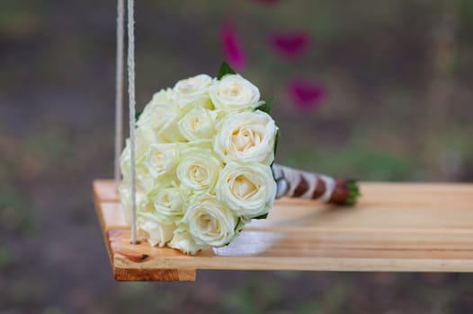 bridal bouquet of white roses lay on a swing