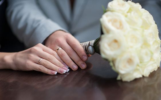 hands of bride and groom with wedding rings and bouquet of roses.
