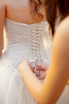 bridesmaid helps the bride to wear dress.
