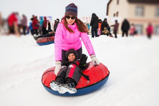 Mother and her son on a snow tube, at beauty winter day