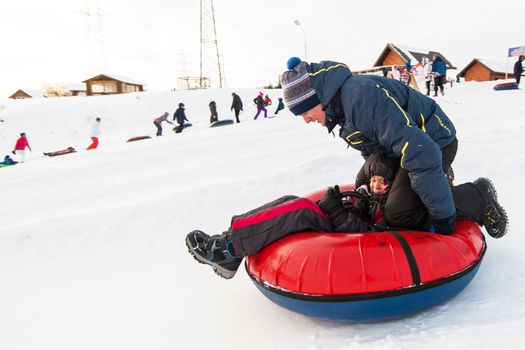 Father and his son having fun on a snow tube, at beauty winter day