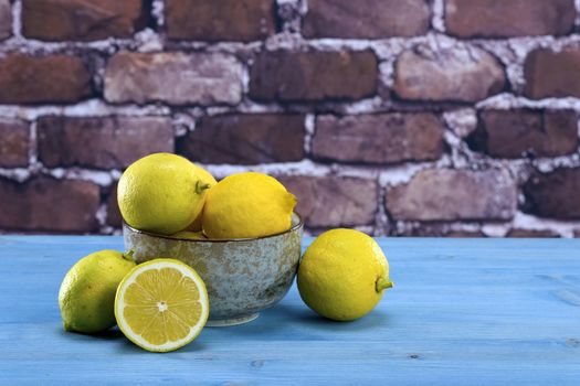 Ripe yellow lemons arranged in a gray bowl. In the background of raw red brick wall.