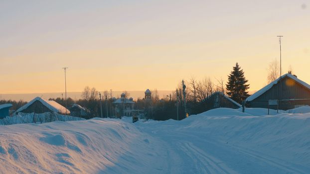 Winter village in a forest. Snow covered roofs of wooden houses, Small old church. Sunset. 4K