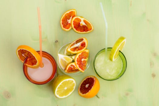 Lemon juice and orange with fruit slices on a green table and red background