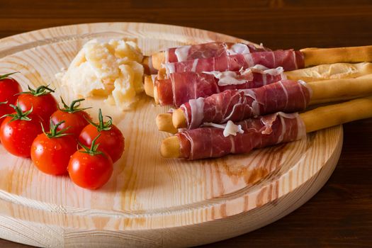Ham rolled in breadsticks cheese and cherry tomatoes over a chopping board