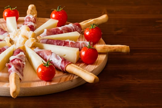 Italian cutting board with ham rolled in bread-sticks cheese and cherry tomatoes