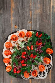 Fresh vegetables, greens and mushrooms on a black ceramic plate in style a rustic