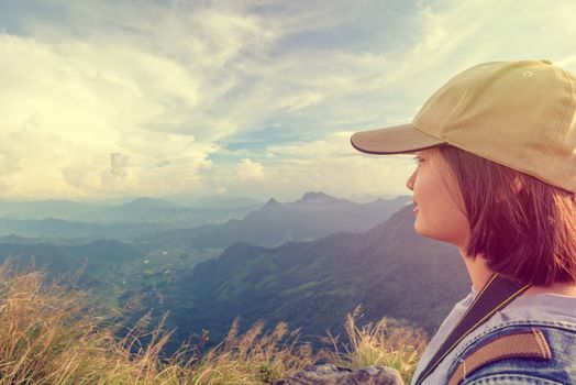 Vintage style hiker asian teen girl wear cap with happy looking beautiful landscape nature on top of high mountain at viewpoint Phu Chi Fa Forest Park, Chiang Rai, Thailand
