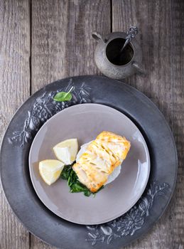 Fried cod fillets and spinach on a wooden surface