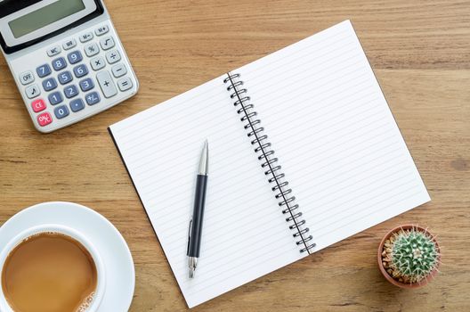 Wooden desk table with notebook, pen, calculator and cup of coffee. Top view with copy space, flat lay.