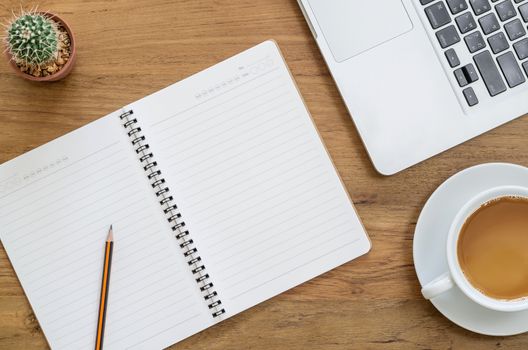 Wooden desk table with notebook, computer laptop, pencil, cactus and cup of coffee. Top view with copy space, flat lay.