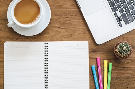 Wooden desk table with notebook, computer laptop, color pen, cactus and cup of coffee. Top view with copy space, flat lay.