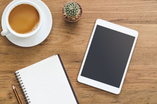 Wooden desk table with tablet, notebook, pencil and cup of coffee. Top view with copy space, flat lay.