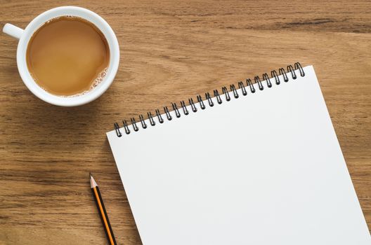 Wooden desk table with notebook, pencil and cup of coffee. Top view with copy space, flat lay.