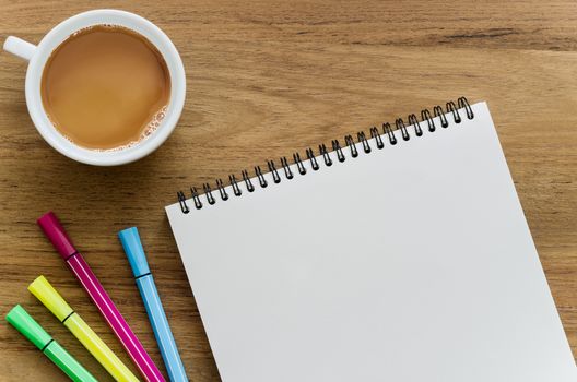 Wooden desk table with notebook, color pens and cup of coffee. Top view with copy space, flat lay.