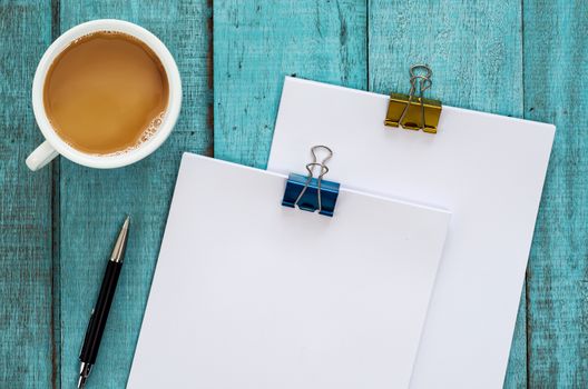 Blue wooden desk table with paper reams, pen and cup of coffee. Top view with copy space, flat lay.