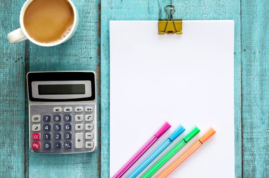 Blue wooden desk table with paper ream, color pen, calculator and cup of coffee. Top view with copy space, flat lay.